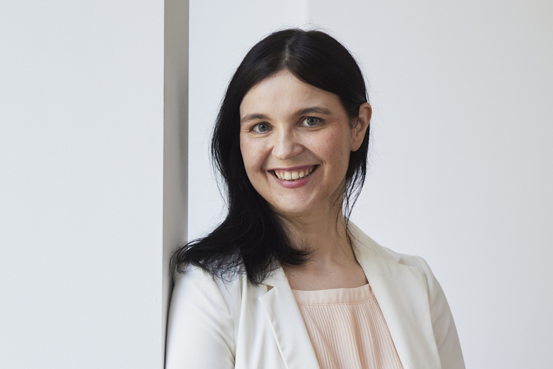 Ana Da Silva is wearing a white jacket and a light pink top. She has black hair and is smiling.